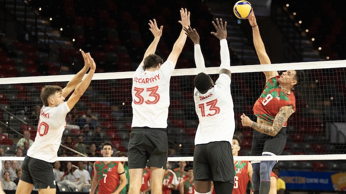 Des joueurs de volleyball en blanc sautent pour effectuer un bloc.