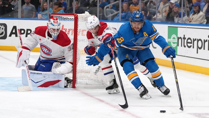 Un hockeyeur tente de contourner un adversaire avec la rondelle à côté du filet adverse. 