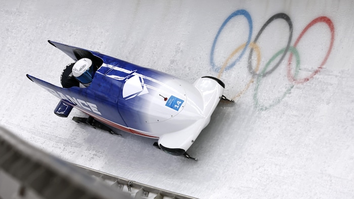 Un bobsleigh dévale une piste sur laquelle se trouve les anneaux olympiques.