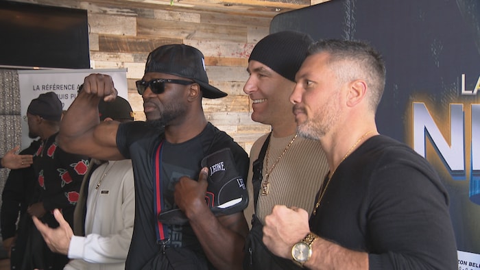 En compagnie de leur promoteur, deux boxeurs posent determination la caméra en serrant le poing.