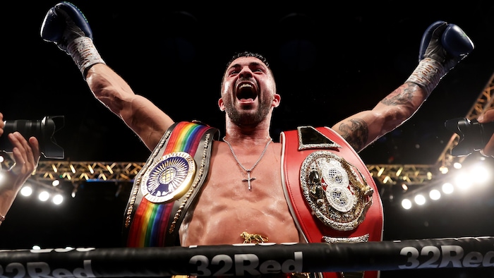 Un boxeur les bras au ciel avec ses ceintures de champion.
