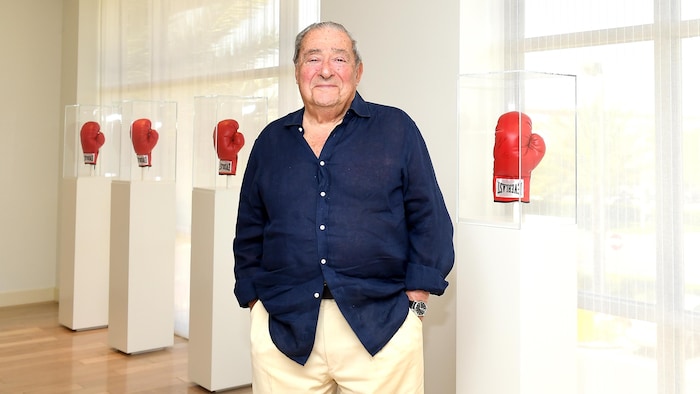 Un homme dans une pièce blanche. Derrière lui, des gants de boxe rouges