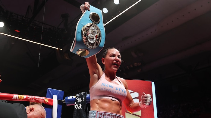 La boxeuse tient une ceinture dans sa main droite dans un ring.