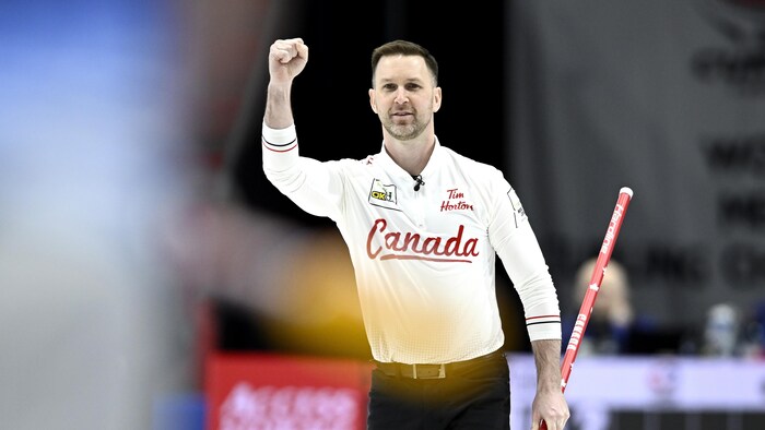 Un joueur de curling tient son balai dans une main et lève le poing de l'autre après une victoire.