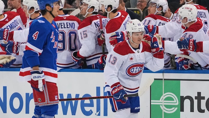 Un hockeyeur célèbre son but avec ses coéquipiers debout au banc des joueurs.