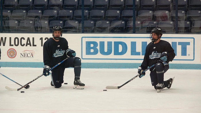 Deux joueurs de hockey agenouillés sur la patinoire.