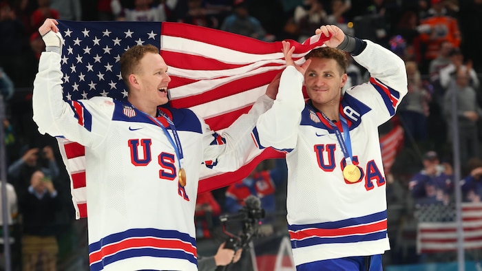 Deux joueurs de hockey célèbrent leur victoire olympique avec un drapeau et leur médaille.