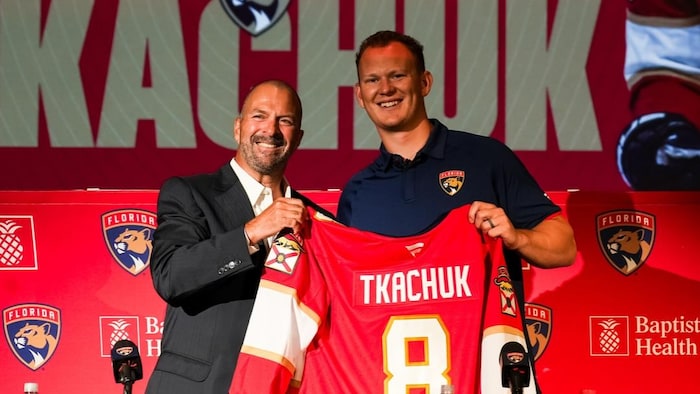 Un joueur de hockey montre son nouveau chandail d'équipe avec son directeur général.