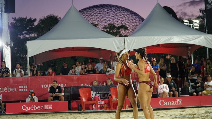 Deux joueuses de volleyball de plage se félicitent, avec au loin la Biosphère.
