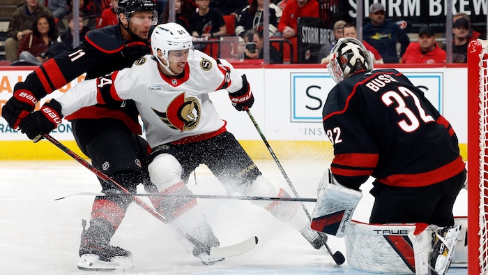 Un gardien de but de hockey effectue un arrêt devant un adversaire qui est poussé par son coéquipier près de sa zone.