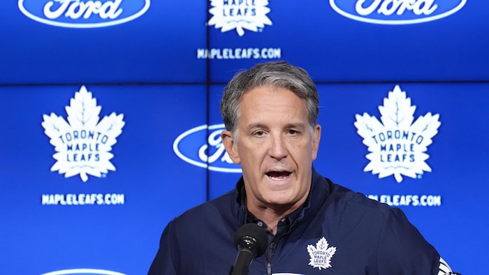 Un homme parle devant un écran bleu avec le signe des Maple Leafs. 