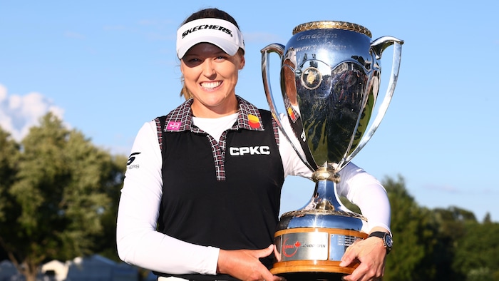 Une golfeuse sourit à pleines dents en tenant un trophée dans ses mains.