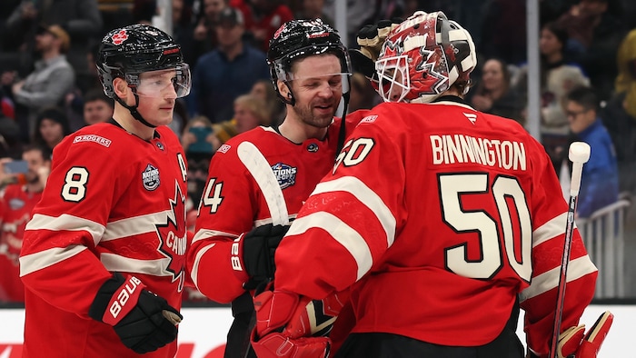Deux hockeyeurs félicitent leur gardien après une victoire.