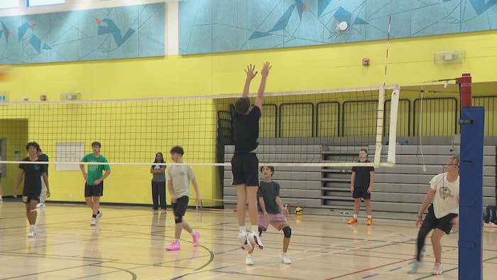 Jeune garçon saute au filet de villeyball. D'autres jeunes le regardent.