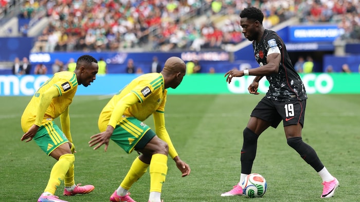 Un joueur de soccer contrôle le ballon devant deux adversaires.