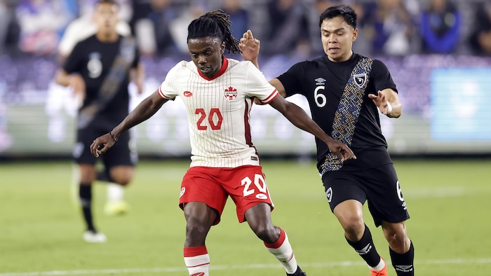 Un joueur de soccer s'apprête à faire une passe tandis qu'un joueur adverse lui met la pression.