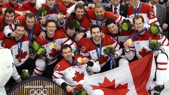 Des joueurs canadiens posent pour une photo avec leur médaille d'or, et le drapeau canadien.