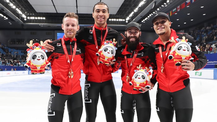 Quatre patineurs avec leurs médailles et leurs peluches sourient pour la photo sur la patinoire.