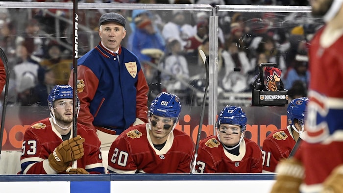 Un entraineur de hockey derrière ses joueurs au banc. 