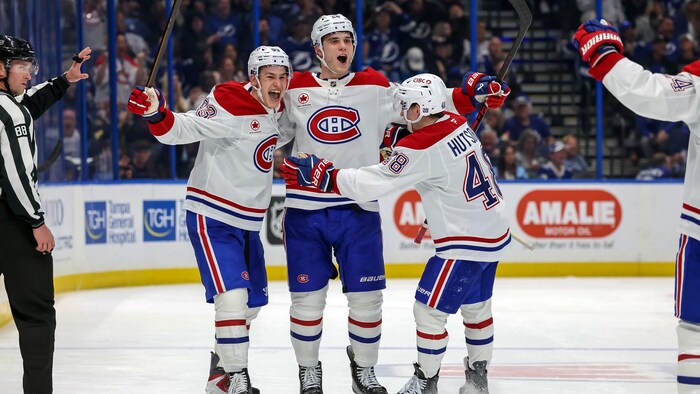 Trois joueurs de hockey en blanc célèbrent un but. 
