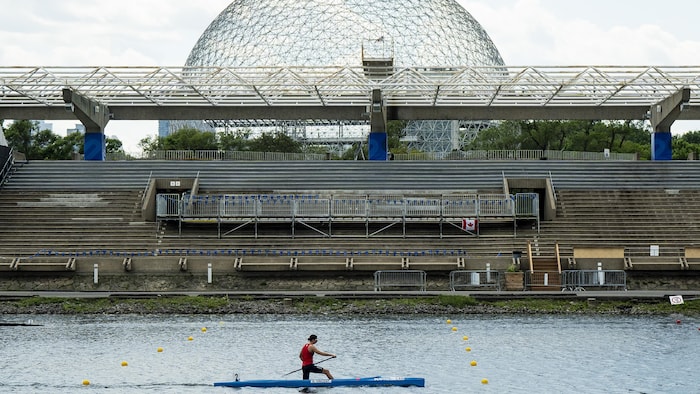 Une canoéiste pagaie avec la biosphère du parc Jean-Drapeau, à Montréal, en arrière-plan.
