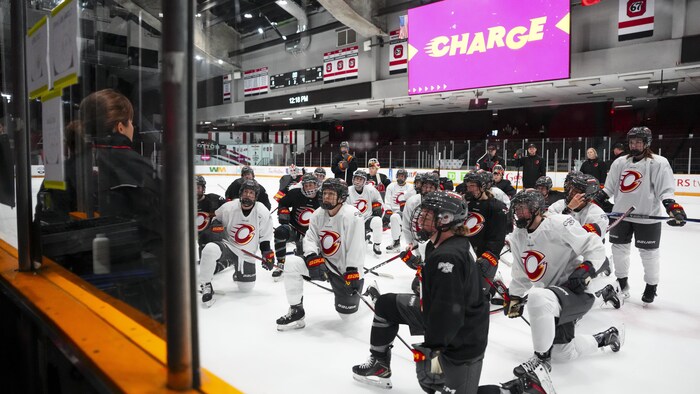 Des joueuses de hockey sont attentives pendant le discours de leur entraîneuse à l'entraînement.