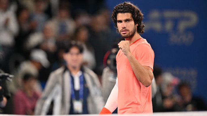 Un joueur de tennis en rose montre le poing avec un air satisfait.