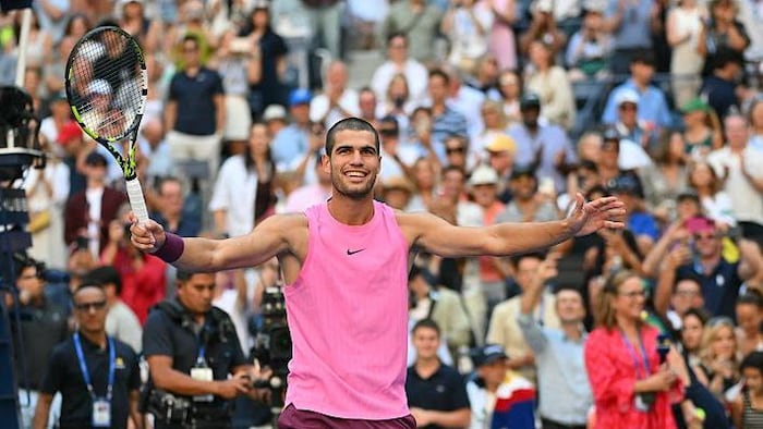 Un joueur de tennis en rose ouvre les bras et sourit à la foule après sa victoire.