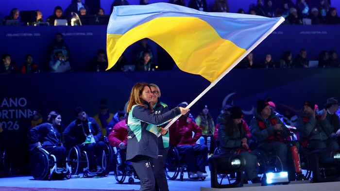 Une bénévole tient le drapeau de l'Ukraine et marche sur la surface du Stade olympique de Cortina pendant la cérémonie de clôture.