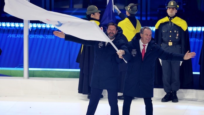 Les présidents des régions de Provence-Alpes-Côte d'Azur et d'Auvergne-Rhône-Alpes tiennent le drapeau paralympique en souriant.