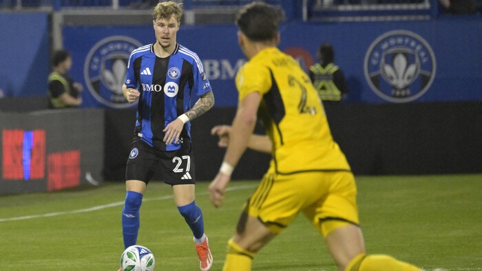Un joueur de soccer contrôle le ballon devant un adversaire. 