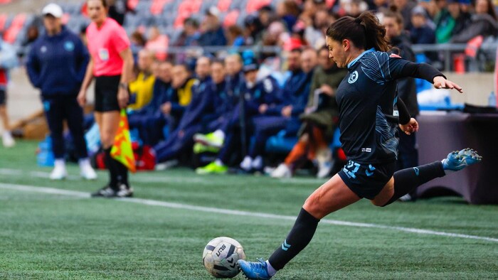 Une joueuse de soccer s'apprête à frapper le ballon sur un coup franc dans un match professionnel.