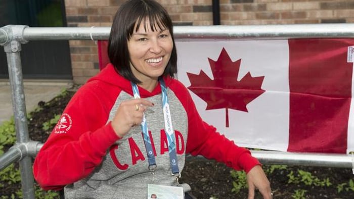 Une femme en fauteuil roulant sourit devant un drapeau canadien.