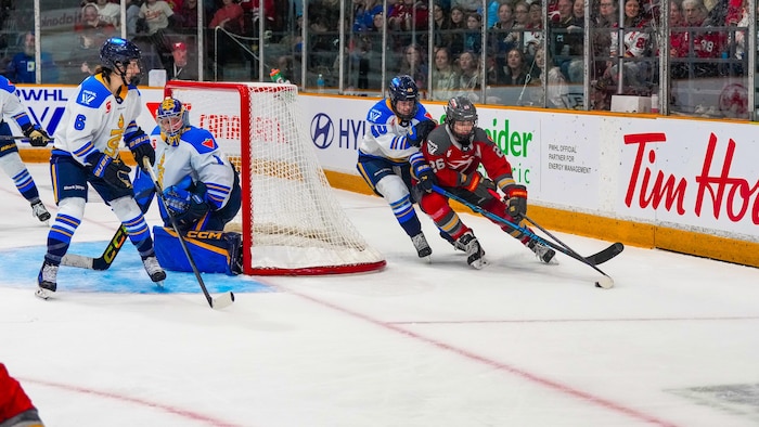 Une joueuse de hockey fait le tour du filet en possession de la rondelle, étroitement surveillée par son adversaire.