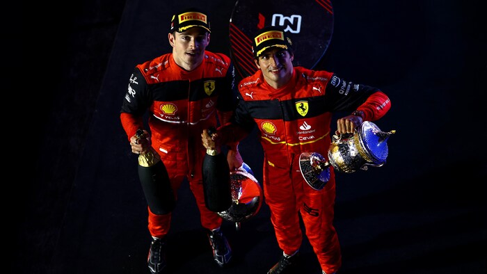 Deux pilotes automobiles tiennent un trophée et une bouteille de champagne.