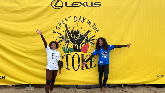Deux surfeuses posent devant une affiche. 
