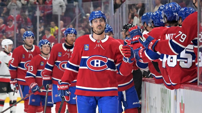 Un hockeyeur célèbre un but avec ses coéquipiers debout au banc des joueurs.
