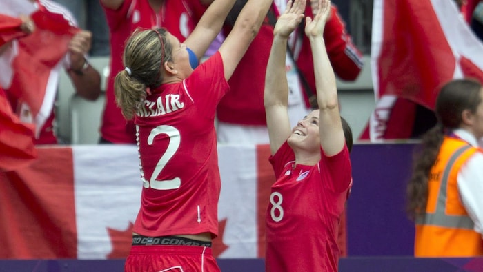 Deux joueuses en rouge, l'une devant l'autre, lèvent les bras au ciel en souriant.