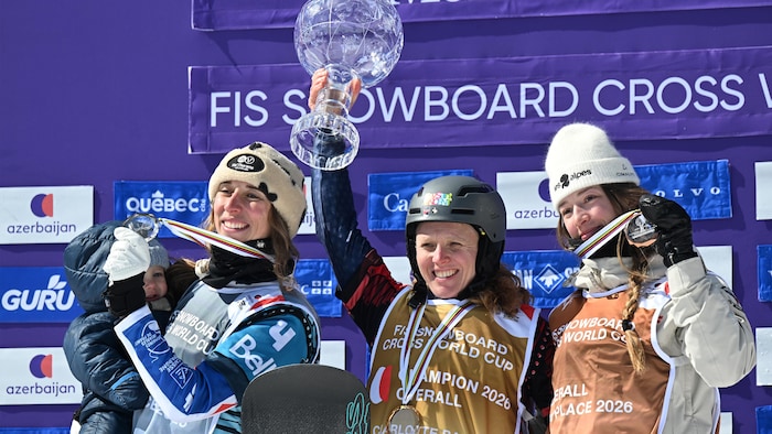 Trois athlètes sur le podium avec leur médaille. Celle du centre lève son globe de cristal dans les airs.