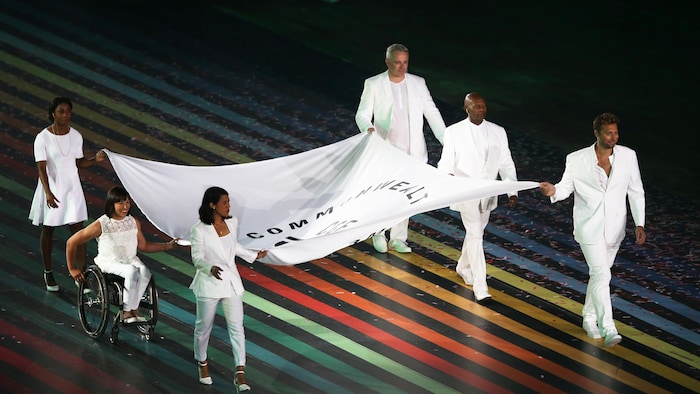 Six personnes, dont une en fauteuil roulant, avancent en tenant un drapeau. 