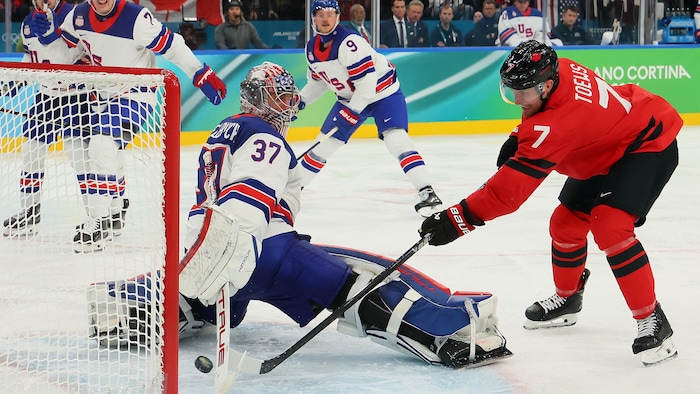 Un gardien de but au hockey étire le bras droit et fait l'arrêt avec son bâton.