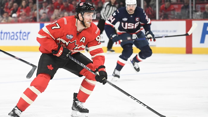 Un joueur de hockey avec la rondelle, un adversaire le pourchasse.