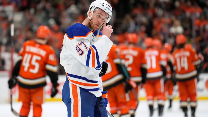 Connor McDavid essuie sa visière alors que derrière lui, les joueurs des Ducks célébrent leur victoire. 