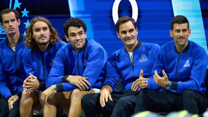 Cinq hommes sont assis sur un banc et regardent un lucifer de tennis.
