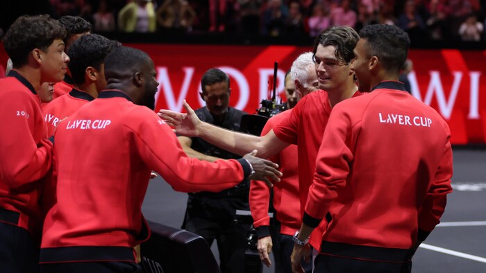Des joueurs de tennis, vêtus d'un uniforme rouge, se donnent la main après une victoire.