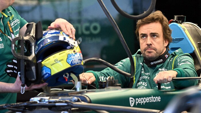 Assis dans sa monoplace, un pilote en vert regarde vers le haut d'un air dubitatif.