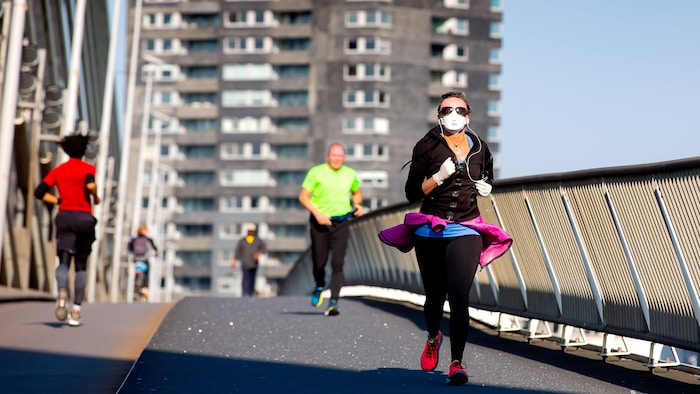 Une femme fait de la course à pied avec un masque et des gants.