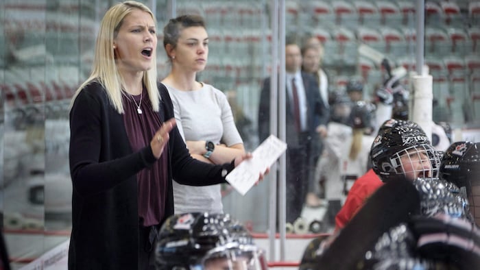 L'entraîneuse Courtney Kessel tape dans ses mains derrière le banc de l'équipe canadienne de hockey féminin.