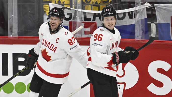 Deux joueurs de hockey, dos à dos, sourient.