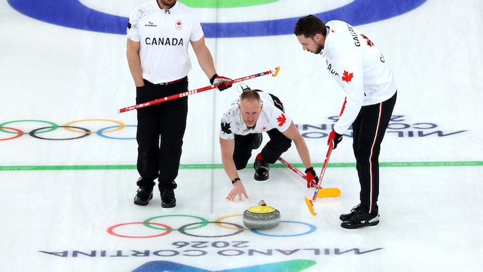 Un capitaine de curling regarde sa pierre avancer pendant un match pendant que ses coéquipiers attendent de balayer.